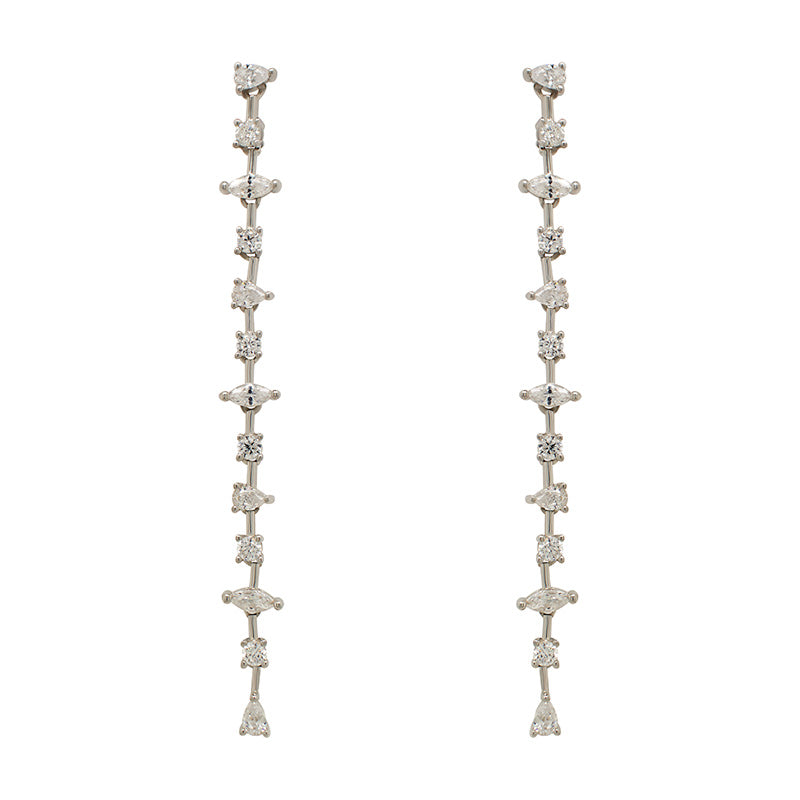 A pair of 925 sterling silver drop earrings with round, pear and marquise cut crystals in front of an ivory colored tile background.