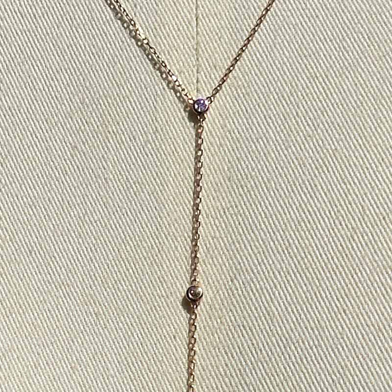 Close up of a lariat style necklace with 9 petite round cut, bezel set diamonds cast in 14 kt rose gold settings on a body form for perspective.