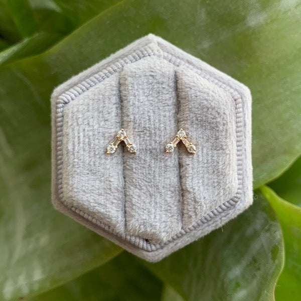 
                  
                    Load image into Gallery viewer, front view of studs with round and baguette diamonds arranged in V. Set in 14 kt yellow gold. Displayed on gray display box in natural light.
                  
                