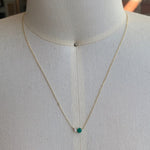 Front view on dress form of an asymmetrical round cut emerald and diamond necklace cast in 14 kt yellow gold.