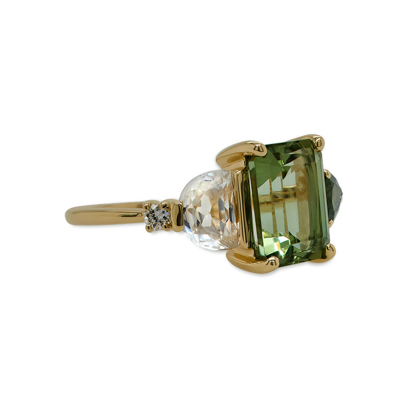 
                  
                    Load image into Gallery viewer, Left side view of an asymmetrical, emerald cut, green tourmaline ring flanked by one half moon cut white sapphire, one pear cut green sapphire, two round cut white diamonds, and cast in 14 kt yellow gold.
                  
                
