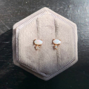 
                  
                    Load image into Gallery viewer, Front view on grey velvet box of white oval opals, set east-west  in 14 kt rose gold with 1 round accent diamond set vertically below each. Photo taken in natural sunlight on light gray velvet earring box.
                  
                