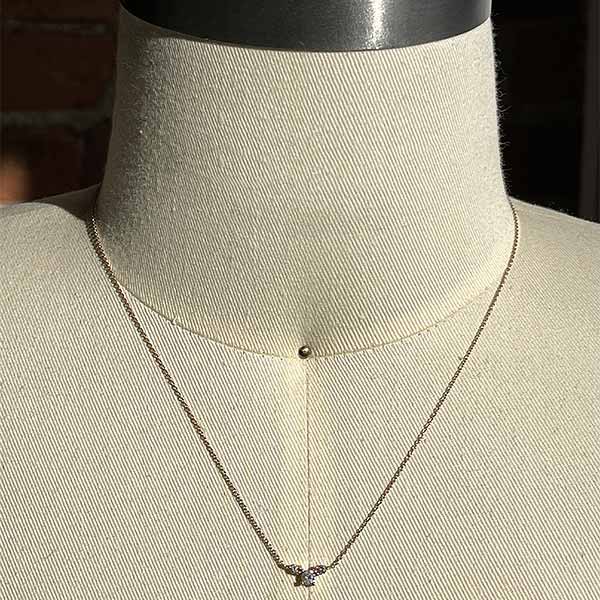 A necklace with three gray diamonds set in a 14 kt yellow gold setting on a dress form for scale.