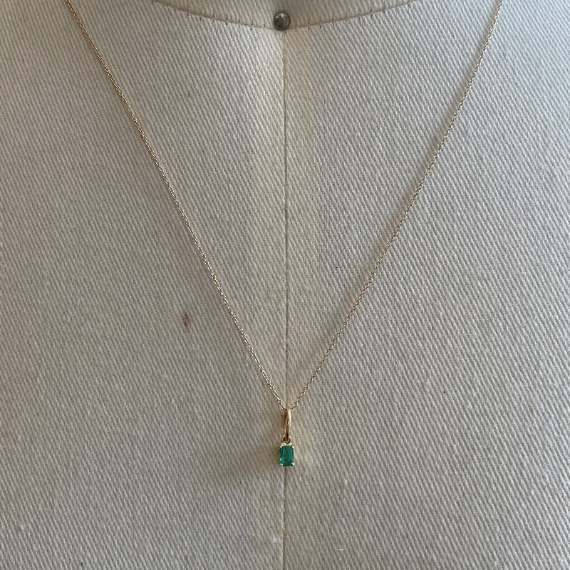 View of .16ct emerald charm on fine gold chain set in 14k yellow gold.