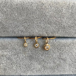 closeup of 3 bezel set diamond charms, in small, medium and large sizes, each set in 14k yellow gold with oversized bails.