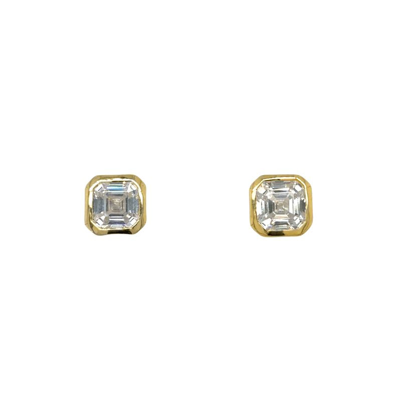 A pair of asscher cut bezel set studs in yellow gold shown on a white background.