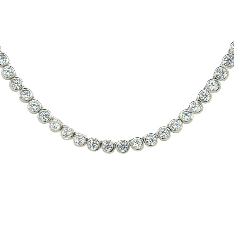 A front view of a tennis necklace with round bezel set stones shown on a white background.