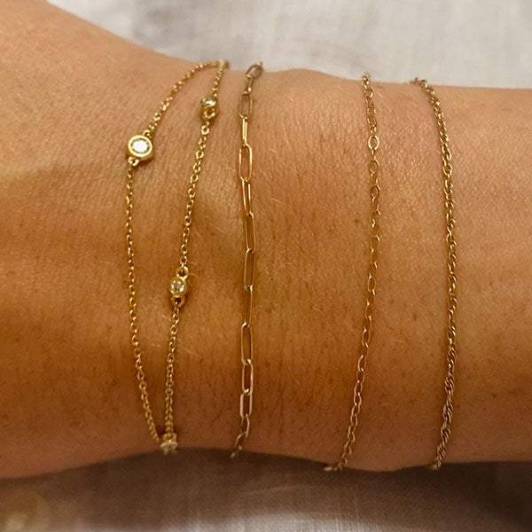 Photo of the wearer's wrist showcasing 5 different styles of 14 kt yellow gold bracelets.