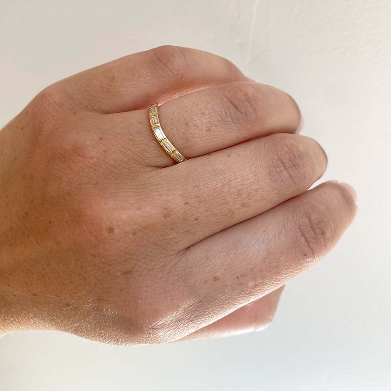 Front view on left ring finger of a shadow band with a slight center dip cast in solid 14 kt yellow gold with 9 bezel set, baguette cut diamonds.