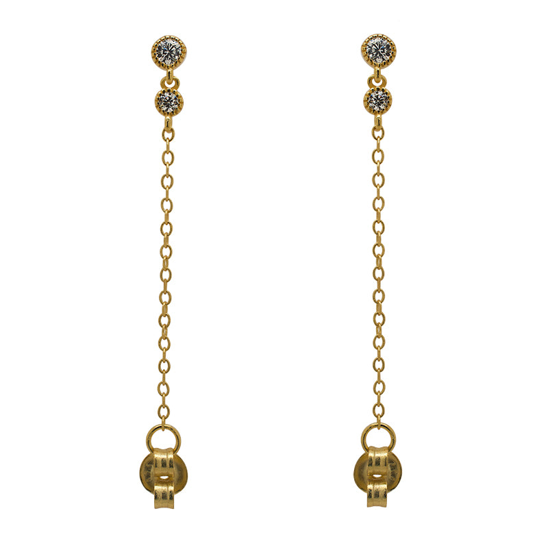 A pair of milgrain, bezel set round crystal studs with a smaller hanging bezel set crystal and chain connected to the earring back, and made of 14 kt yellow gold vermeil.