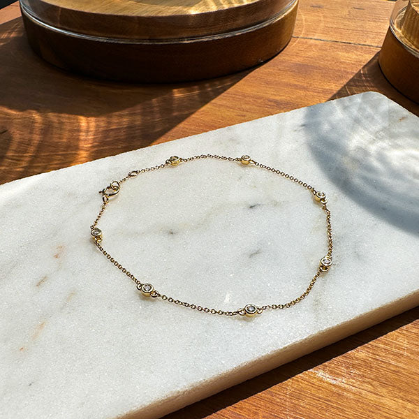 Overview shot of a bezel set 7 diamond bracelet made of solid 14 kt yellow gold on top of an ivory tile resting on a wooden tabletop.
