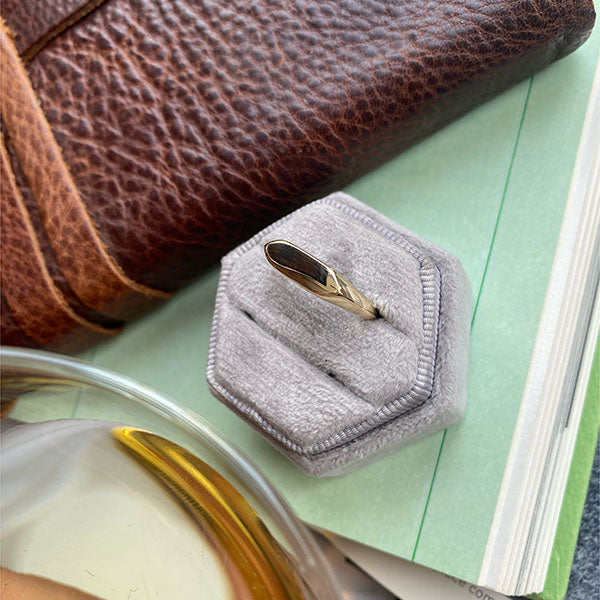 Overview shot of a high polish 14 kt yellow gold signet ring in a ring box on top of a sea foam colored book and leather notebook.