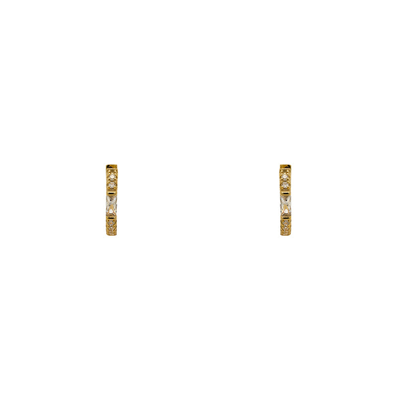 A pair of huggie style earrings with round and baguette crystals in a 14 kt yellow gold vermeil setting. Displayed forward facing on a white background.
