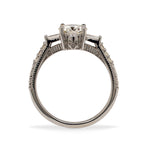 Side view of a round cut diamond engagement ring made of 14 kt white gold with baguette and round cut diamonds going down the shank and a skull engraved on the side.