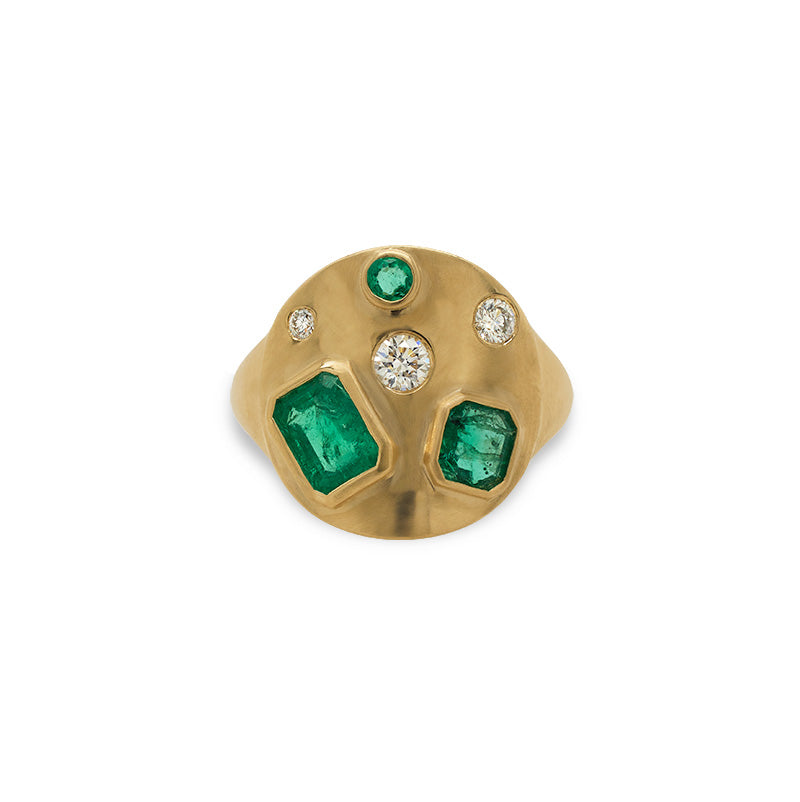 Front view of a signet style ring cast in 14 kt yellow gold with a matte finish, sprinkled with 3 different sizes of round cut diamonds, 1 round cut emerald, one asscher cut  and one emerald cut emerald on a white background.