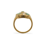 Through the finger view of a signet style ring cast in 14 kt yellow gold with a matte finish, sprinkled with 3 different sizes of round cut diamonds, 1 round cut emerald, one asscher cut and one emerald cut emerald on a white background.