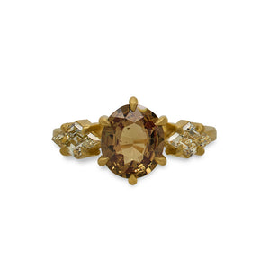 
                  
                    Load image into Gallery viewer, Front view of an oval cut, orange sapphire ring with 2 lozenge cut diamonds set on either side of the sapphire, and set in a claw prong 18 kt yellow gold setting with a matte finish on a white background. 
                  
                