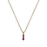 A dainty 14 kt yellow gold necklace with a pendant that has 3 small, round cut rubies in a north south setting on a white background.
