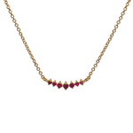 Front view of a small sized 7 stone graduated ruby pendant necklace cast in 14 kt yellow gold.