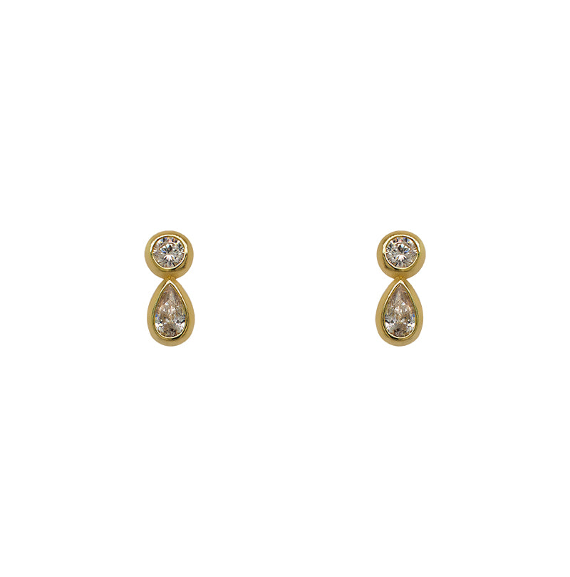A pair of 14 kt yellow gold vermeil stud earrings with one bezel set round crystal and one larger bezel set pear cut crystal on a white background.