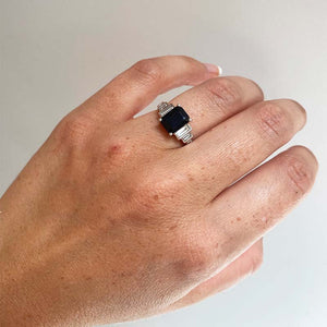 
                  
                    Load image into Gallery viewer, Front view  on left ring finger of emerald cut black sapphire ring with 6 baguette cut diamonds set in 14 kt white gold.
                  
                