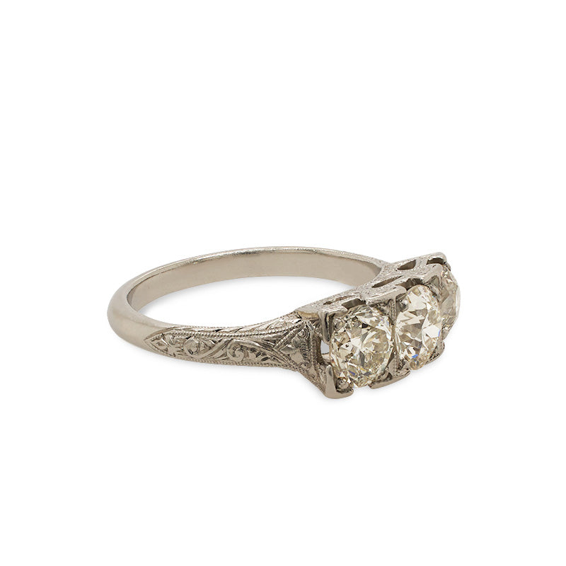 
                  
                    Load image into Gallery viewer, Side view of an Edwardian Deco style ring with 1 old euro cut center diamond set between 2 old mine cut diamonds. The ring is cast in platinum with a vintage style engraving going down the band.
                  
                