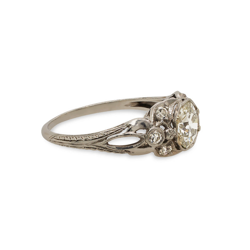 Side view of an Edwardian Deco style ring with 1 old euro cut center diamond set among 6 single cut diamonds. The ring is cast in platinum with a vintage style engraving going down the band.