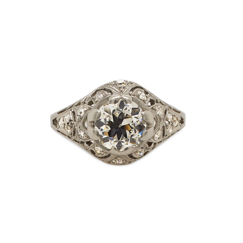 Front view of an Edwardian deco style ring cast in platinum with highly detailed engravings and milgrain throughout with a large old European cut center stone and surrounded by approx 0.25 carats of single cut diamonds.