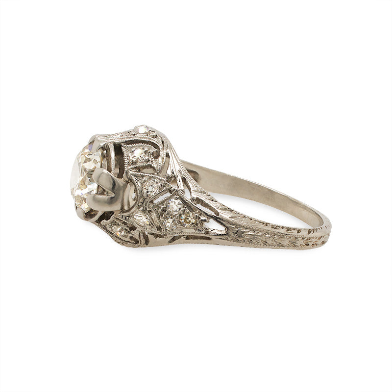 Side view of an Edwardian deco style ring cast in platinum with highly detailed engravings and milgrain throughout with a large old European cut center stone and surrounded by approx 0.25 carats of single cut diamonds.