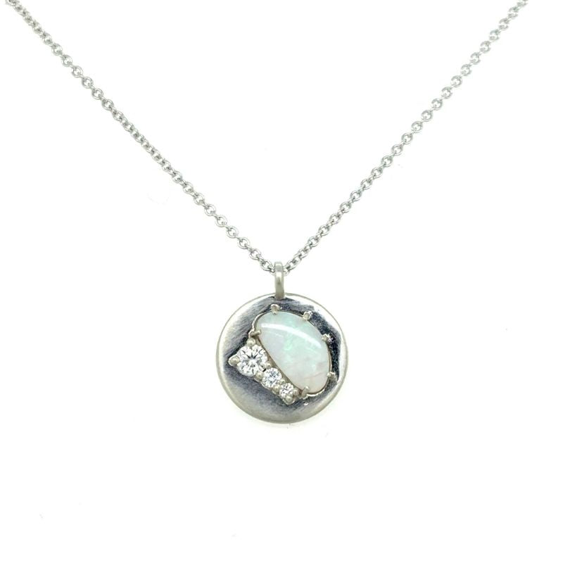 A front view of a white gold pendant with an opal and three round diamonds shown on a white background.