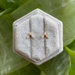 front view of studs with round and baguette diamonds arranged in V. Set in 14 kt yellow gold. Displayed on gray display box in natural light.