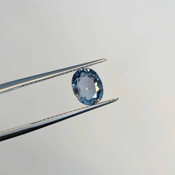 
                  
                    Load image into Gallery viewer, View of a 1.68 ct. blue oval sapphire in tweezers.
                  
                