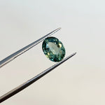 View of an oval 2.06 ct. blue-green sapphire in tweezers.