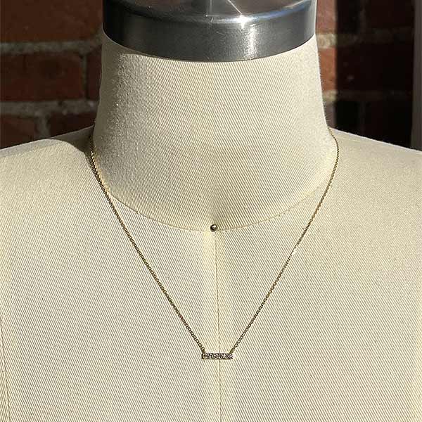 
                  
                    Load image into Gallery viewer, A solid 14 kt yellow gold bar necklace with 5 round cut diamonds on a body form for scale.
                  
                