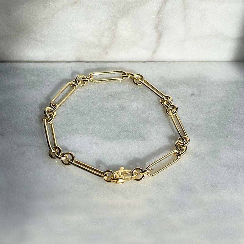 
                  
                    Load image into Gallery viewer, Overhead view of a paperclip and triple ring style bracelet made of solid 14 kt yellow gold with a lobster claw style closure.
                  
                