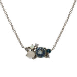 Front view of a round cut aquamarine, moonstone, blue topaz, opal, and diamond cluster necklace cast in 14 kt white gold.