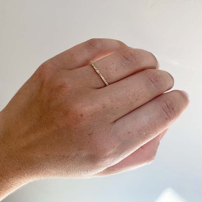 Front view on left ring finger of an asymmetrical diamond band with a 0.14 tcw of round and baguette cut diamonds cast in 14 kt yellow gold.