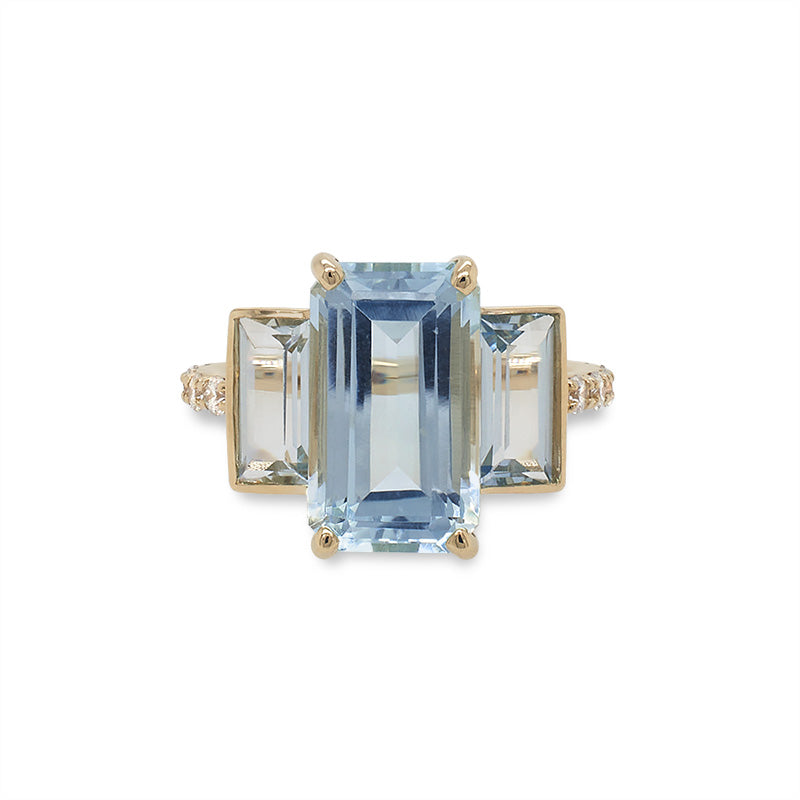 Front view of a triple stone, light blue aquamarine ring with emerald and baguette cuts and round diamonds going half way around the shank and cast in 14 kt yellow gold.