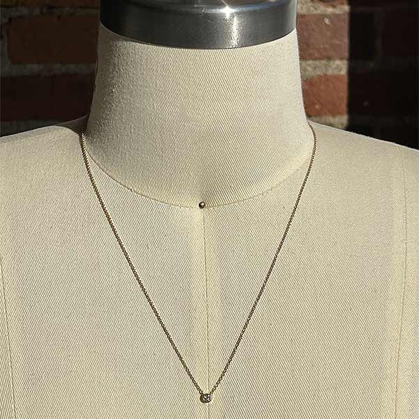 
                  
                    Load image into Gallery viewer, A bezel set diamond solitaire pendant necklace cast in 14 kt yellow gold on a dress form.
                  
                