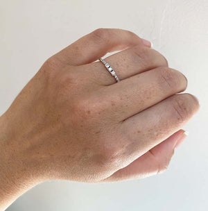 
                  
                    Load image into Gallery viewer, A diamond ring with 3 center round cut diamonds flanked by 6 round cut pavé set diamonds cast in 14 kt white gold on wearer&amp;#39;s left ring finger for scale.
                  
                