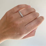 View of 0.90 tcw pavé set eternity band on left ring finger, and cast in 14 kt white gold.