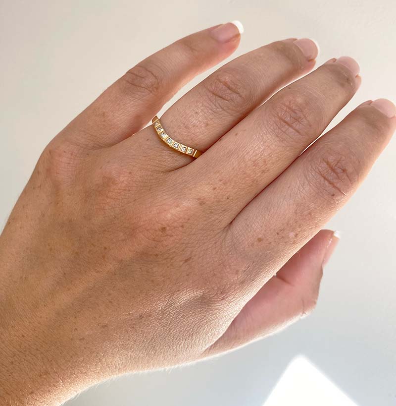 View of a princess cut diamond shadow band on wearer's left ring finger with 7 princess cut diamonds with a tcw of 0.11, and cast in 14 kt yellow gold.