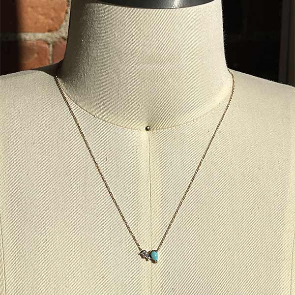 A necklace featuring two round cut diamonds set to one side of a pear cut turquoise stone set in 14 kt yellow gold on a body form.