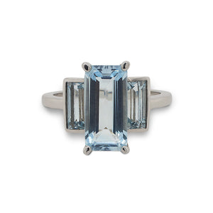 
                  
                    Load image into Gallery viewer, Front view of a three stone aquamarine ring with one larger, emerald cut center stone flanked by two baguette cut stones set in a 14 kt white gold setting.
                  
                