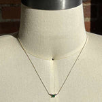 A round cut double diamond and round cut emerald pendant necklace cast in 14 kt yellow gold on a body form.
