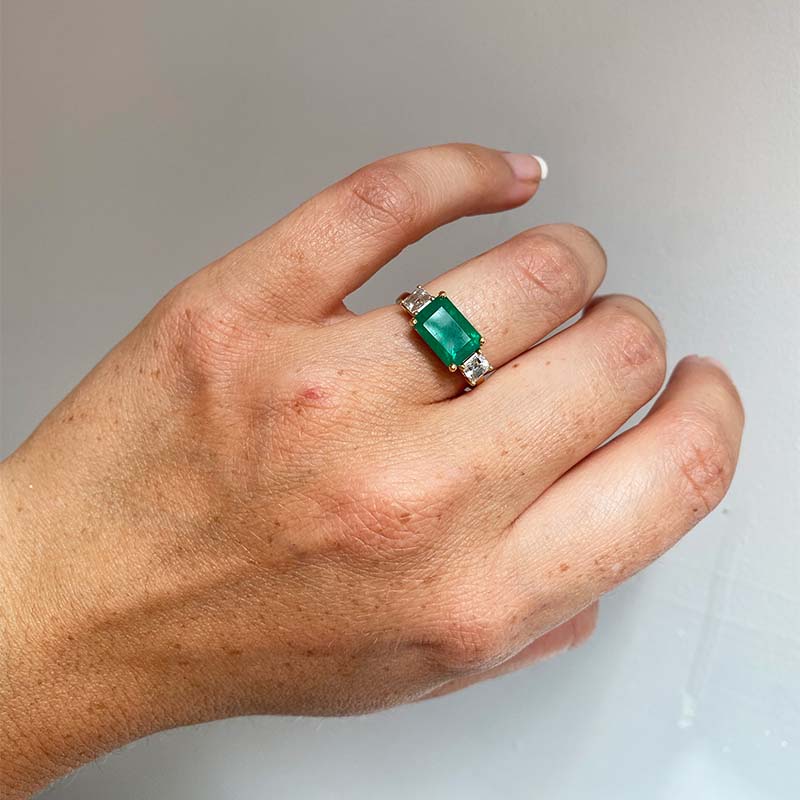 
                  
                    Load image into Gallery viewer, Front view on left ring finger of Columbian emerald ring flanked with 2 asscher cut diamonds set in 14 kt yellow gold.
                  
                