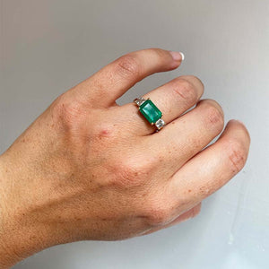 
                  
                    Load image into Gallery viewer, Front view on left ring finger of Columbian emerald ring flanked with 2 asscher cut diamonds set in 14 kt yellow gold.
                  
                