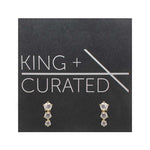 A pair of vertically stacked, triple crystal studs set in 14 kt yellow gold vermeil settings on King and Curated packaging.