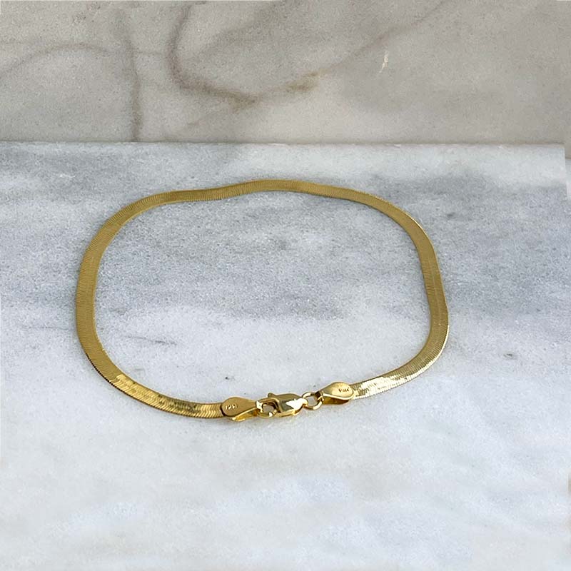 Overhead view of a classic herringbone style gold bracelet made of solid 14 kt yellow gold with a lobster claw style closure.
