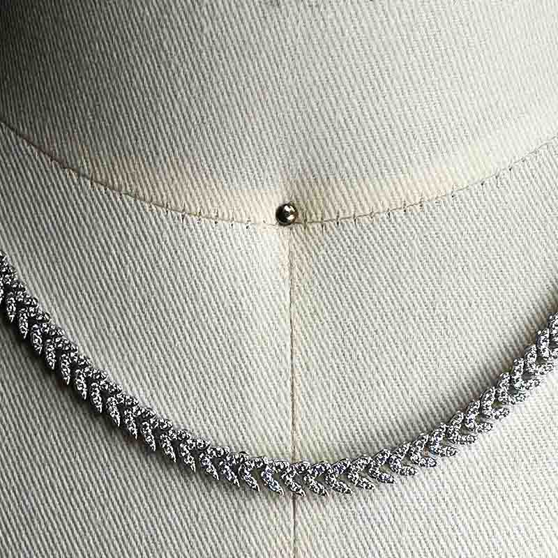 Close up of a pavé set crystal necklace in a sterling silver herringbone style setting on a body form for scale.